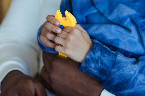 African American father with sin in hands playing with yellow toy adjustable wrench while spending time together in living room