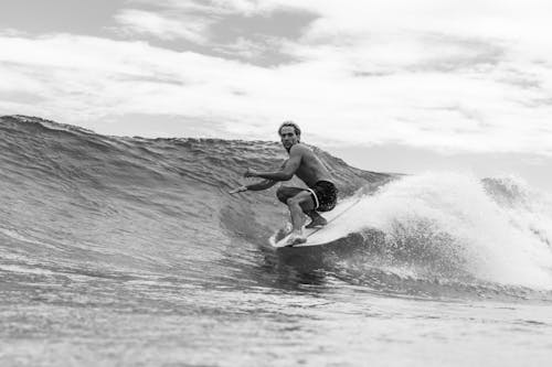 Grayscale Photo of a Shirtless Man Surfing on Sea Waves