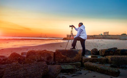 Man Holding a Camera while Taking Picture of Sunset