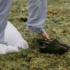 Dark soft backless slippers on moss beside a white duvet