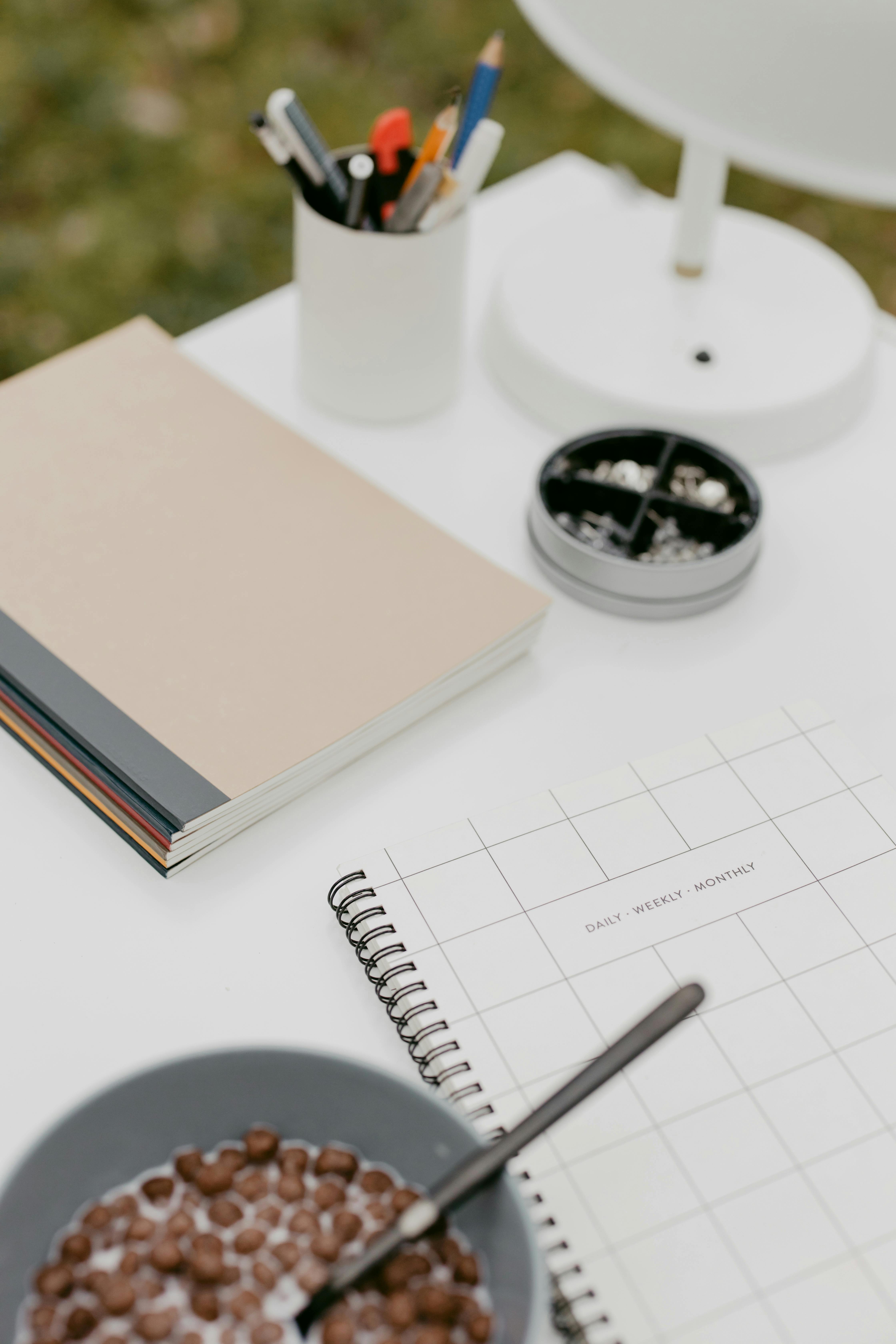 Un espacio de trabajo moderno con cuadernos, cereales y artículos de oficina en un escritorio blanco.