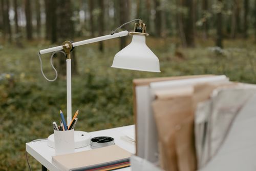 Free White desk lamp and books on a table in a lush forest. Ideal for nature-inspired workspaces. Stock Photo