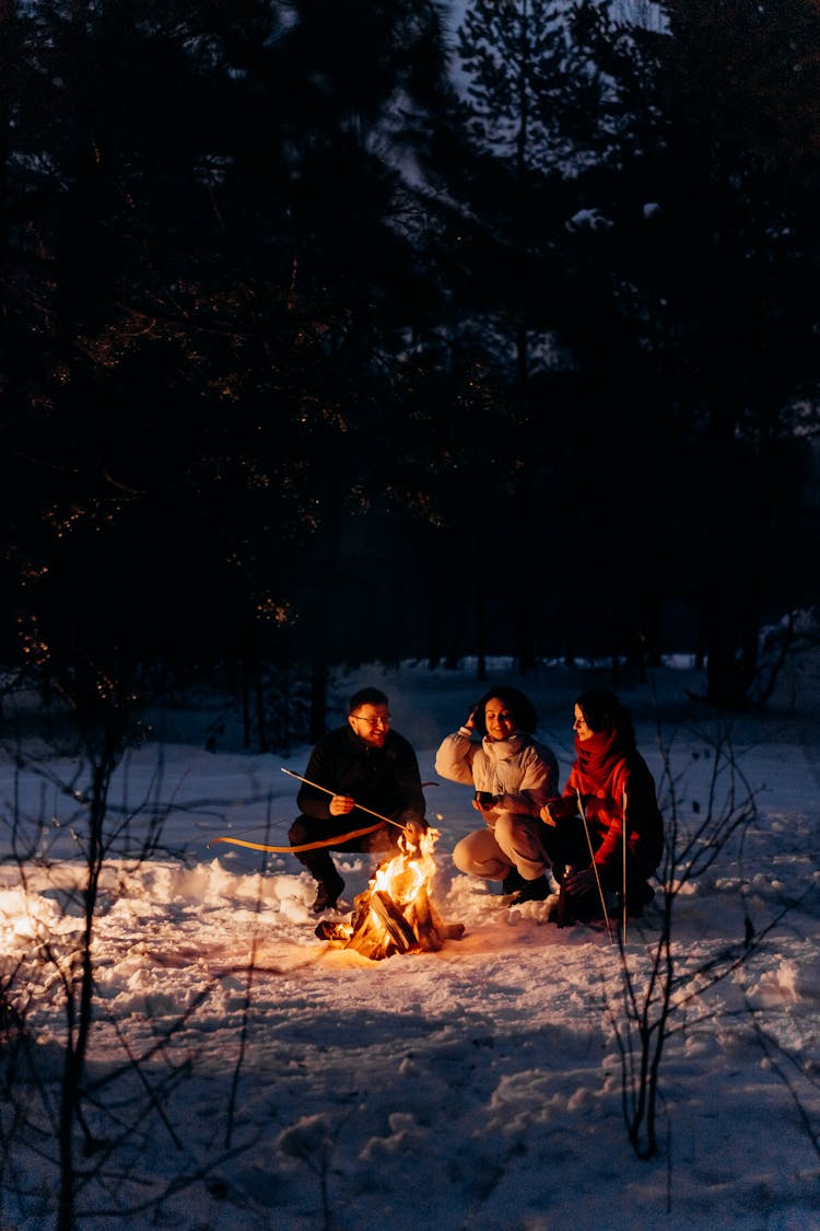 Man And Women Sitting On Snow Beside A Bonfire