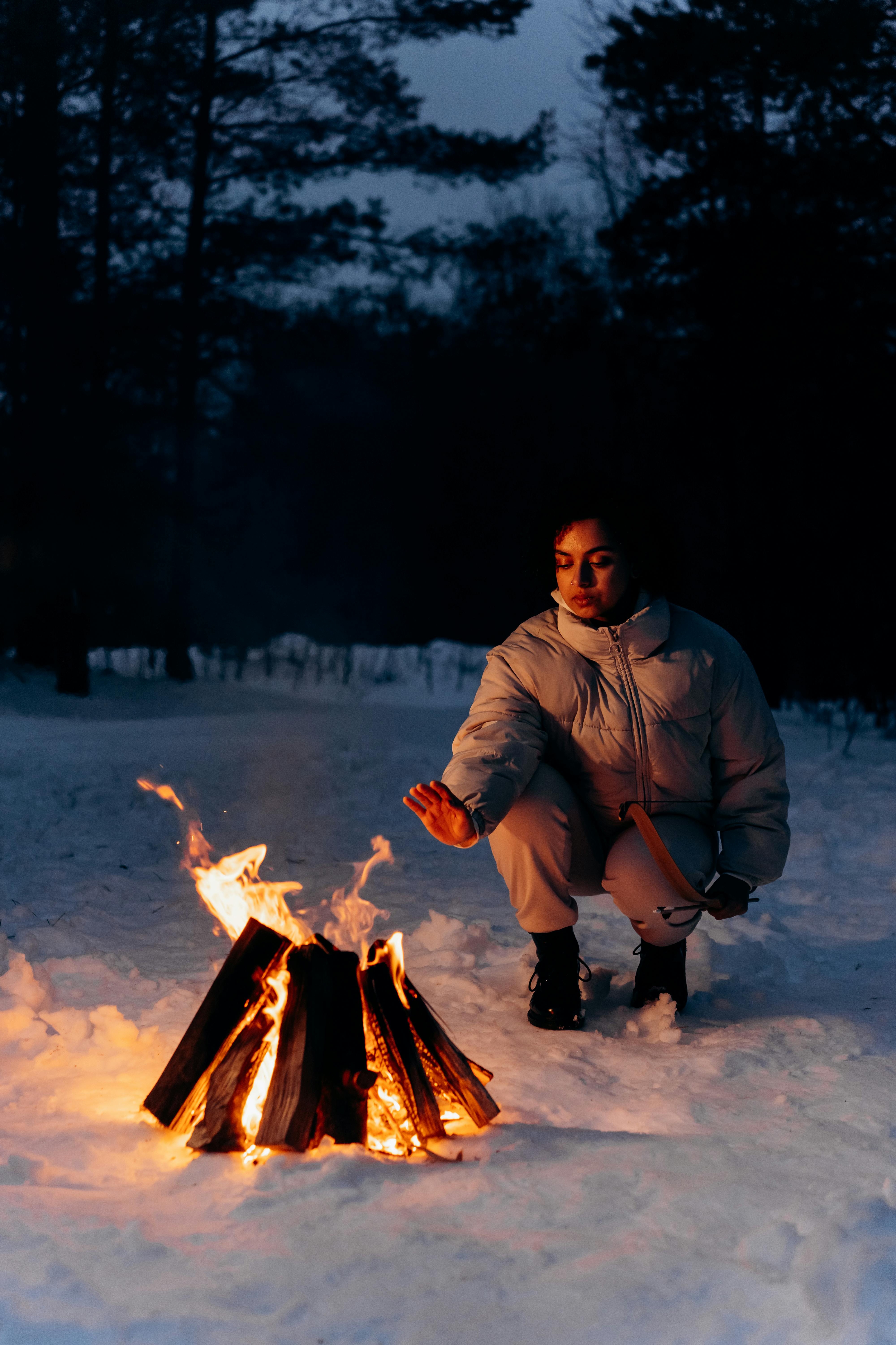 woman placing hand over a bonfire to keep warm