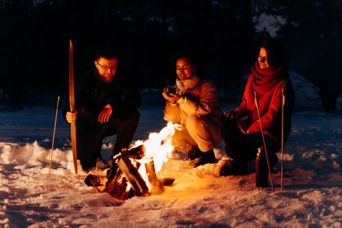 Free Three friends enjoying a campfire in a snowy winter setting. Warmth in winter. Stock Photo