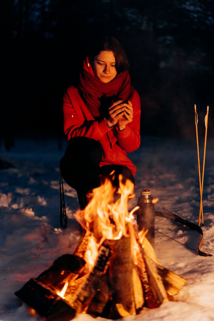 Woman In Red Jacket Sitting Beside A Bonfire