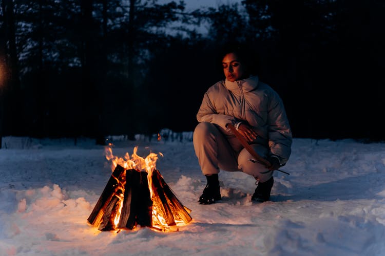 Woman Squatting Beside A Campfire