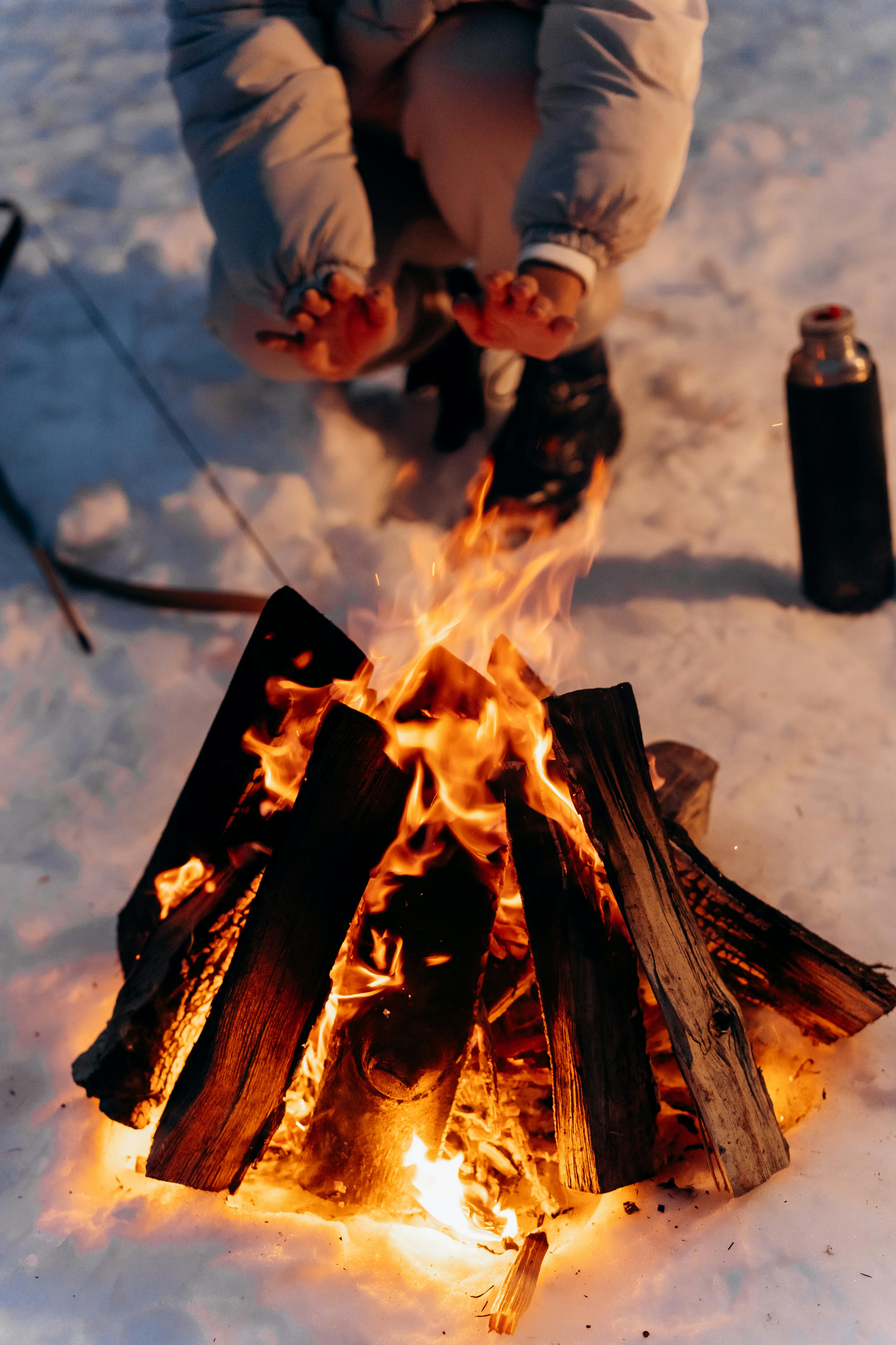 close up photo of a person getting heat from a campfire