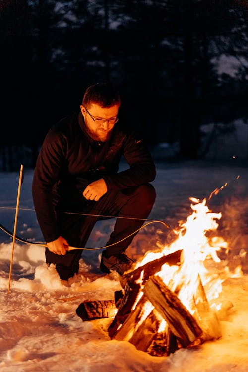 Free Photo of a Man in Black Clothes Kneeling Near a Campfire Stock Photo