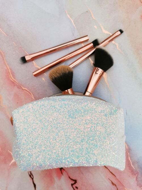 Free Shimmering makeup pouch with brushes on marble background. Perfect for beauty enthusiasts. Stock Photo