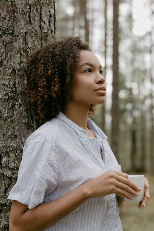 Woman Holding a Drink While Leaning on a Tree