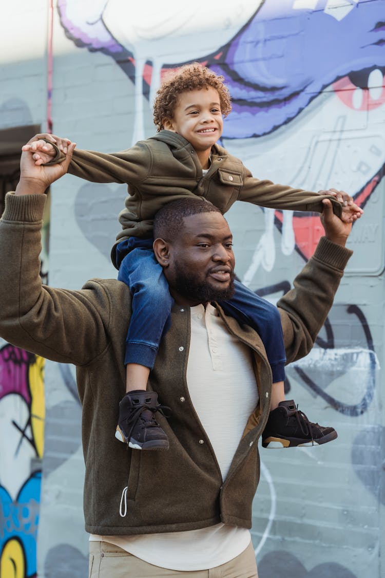 Cheerful Black Father With Son On Shoulders