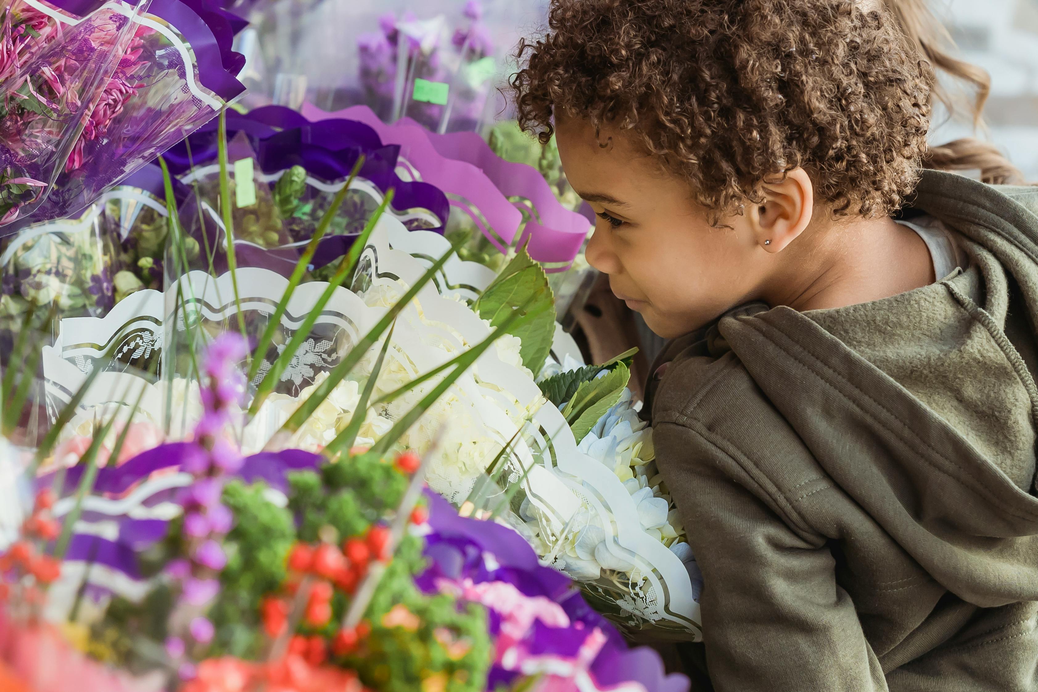 crop cute black boy smelling aromatic flowers in floral store