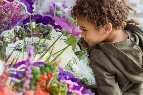 Crop cute black boy smelling aromatic flowers in floral store