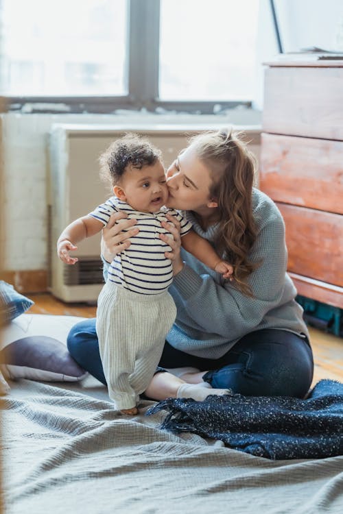 Loving mother kissing ethnic baby on floor