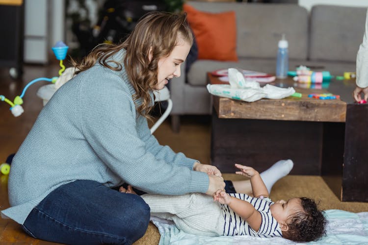 Happy Mother Putting Pants On Baby Lying On Floor