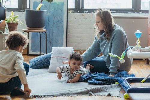 Free Positive mother playing with ethnic kids while sitting on floor in light living room Stock Photo
