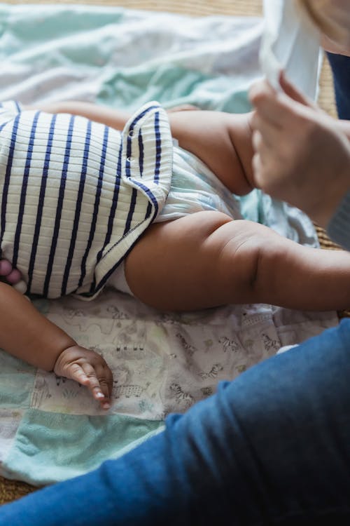Free From above of crop anonymous mom putting on African American child diaper lying on floor Stock Photo