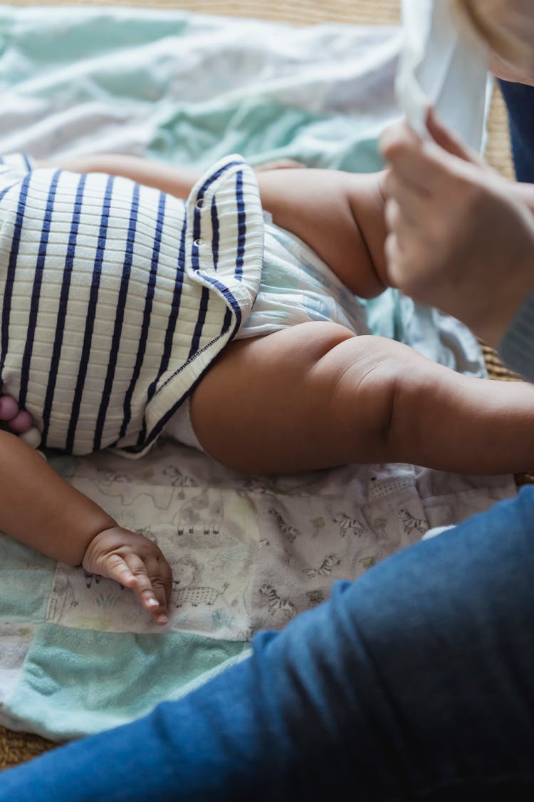 Mother Changing Diaper For Black Baby Lying On Blanket