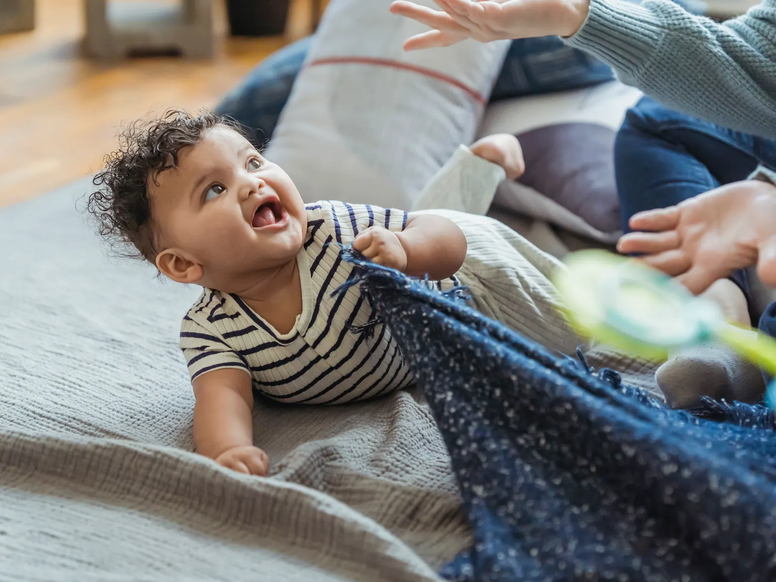 Baby lying on a plaid blanket with mouth open, mother sitting close nearby