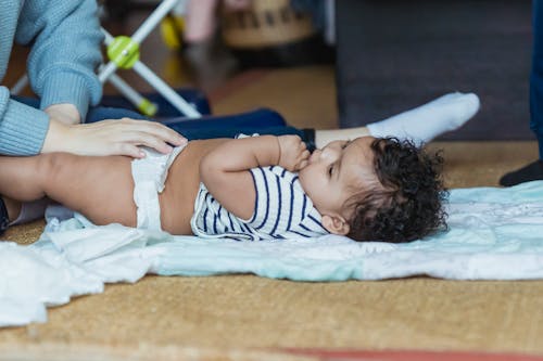 Free Side view of adorable little African American baby lying on floor with crop mom changing diaper Stock Photo