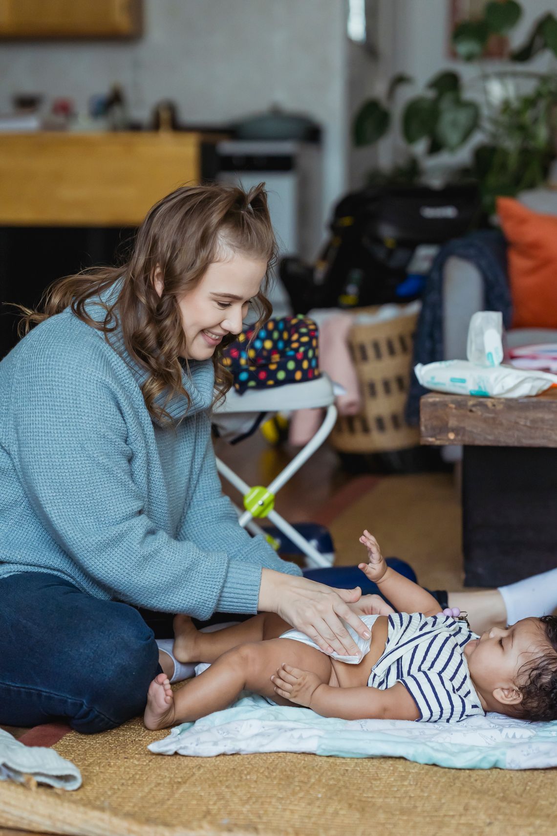 Smiling mother changing her baby's diaper on the floor, with her face clearly visible