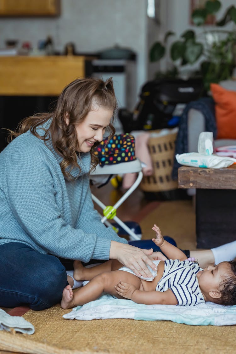 Mother Changing Diaper For Black Baby Lying On Floor