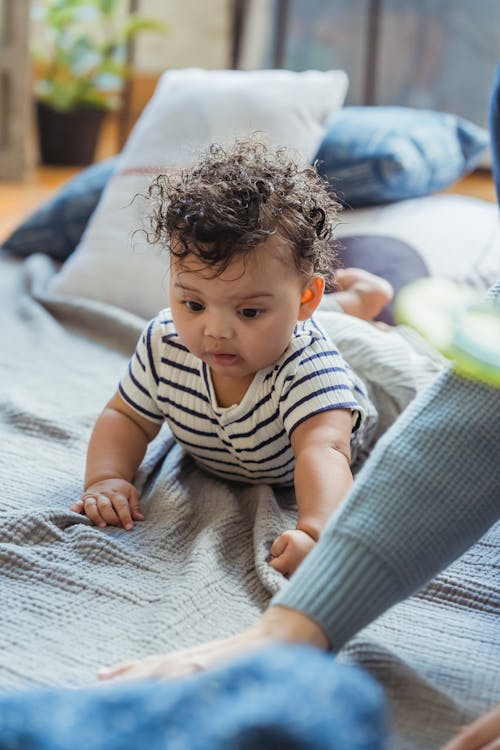 Free Curious African American infant with curly hair crawling on plaid near crop mother Stock Photo