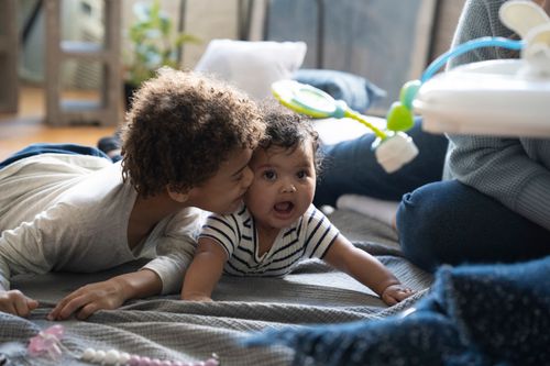 Free Adorable gentle African American boy caressing baby while lying on floor with crop mother Stock Photo