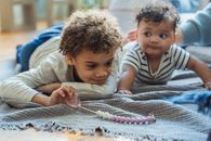 Cute black boy with nipple in hand lying near baby