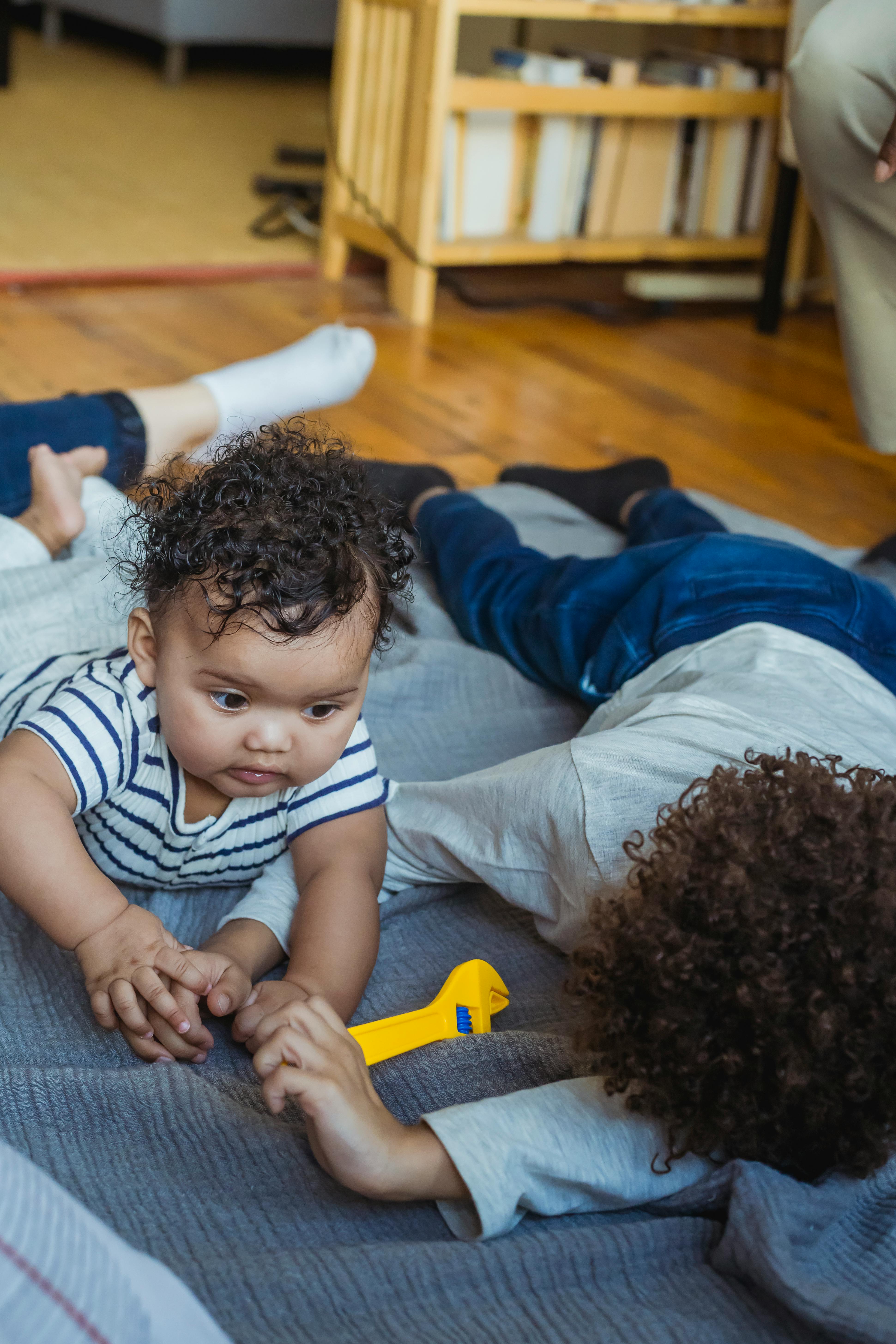 little boy playing with baby while lying on floor