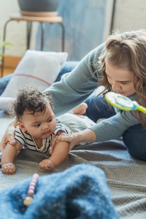 Free High angle of gentle mother sitting on floor near African American baby crawling on plaid Stock Photo