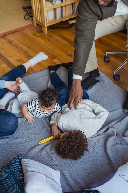 Black father tickling son lying on floor with baby