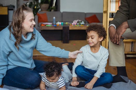 Cheerful mother holding hand of black awkward son sitting near baby and crop father at home
