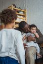 Back view of elder child standing in living room and looking at dad embracing little brother and speaking in ear