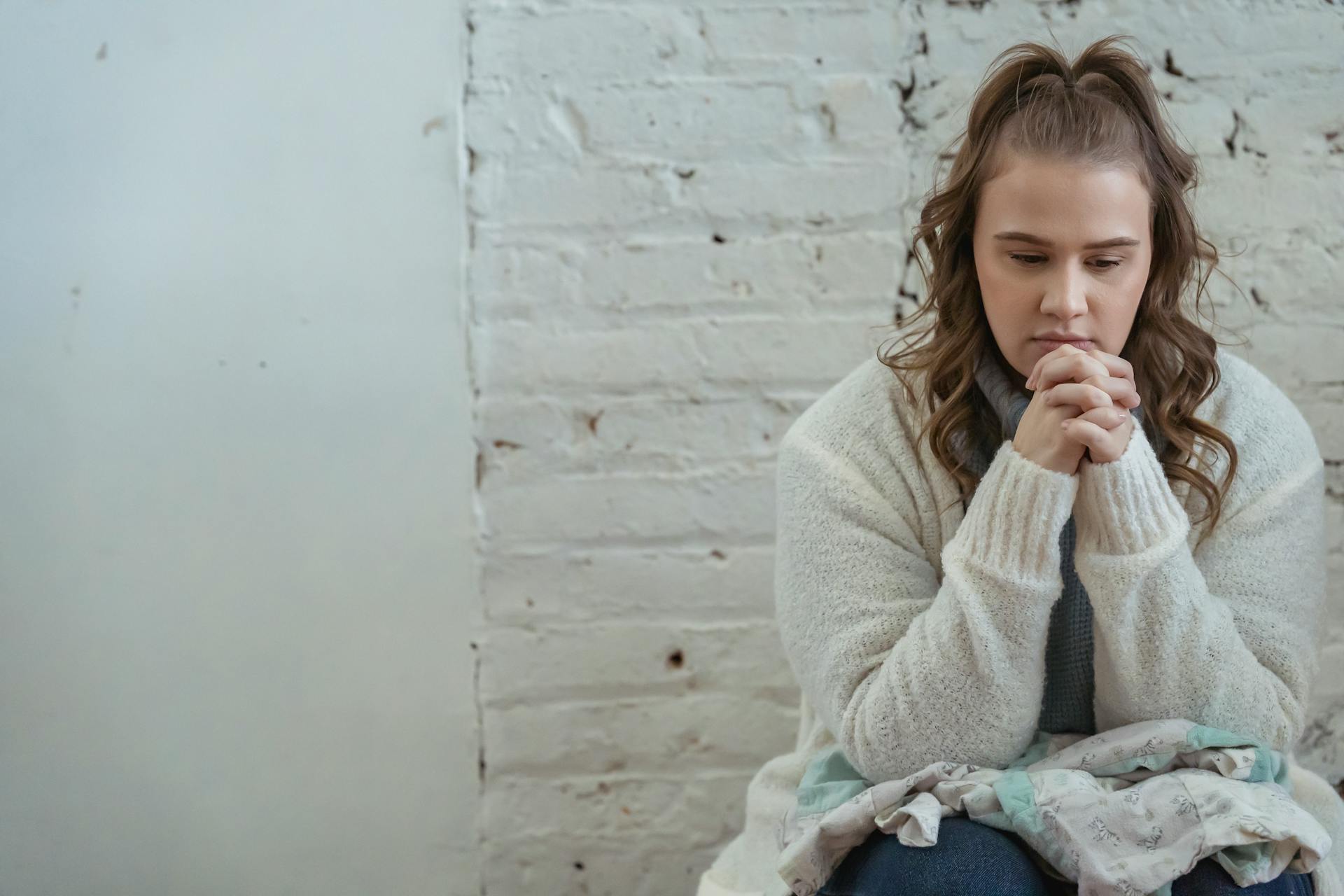 Young pensive female sitting near white wall and pondering unpleasant situation of argument with husband