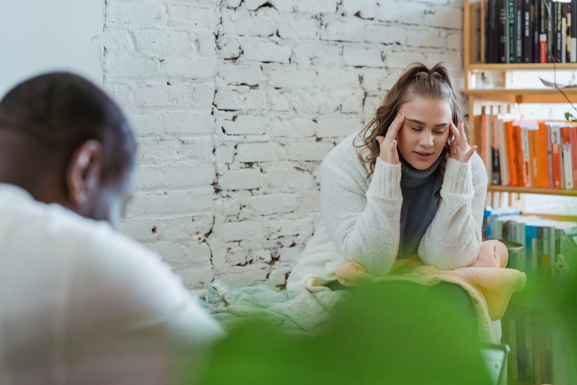 Free Exhausted woman calming down after argument with husband by putting fingers on temples and man sitting and looking down Stock Photo