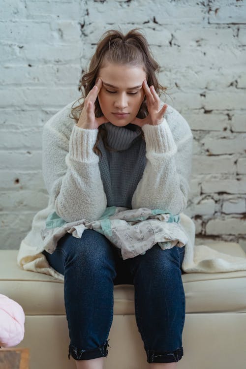 Exhausted female with closed eyes in casual clothes leaning on knees and trying to calm down