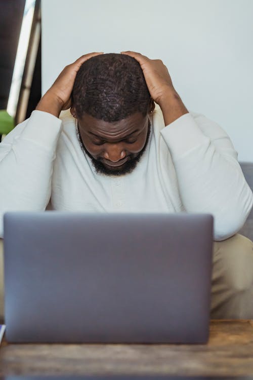 Black man lowering head sitting in front of laptop
