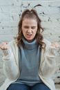Tensive female in warm sweater sitting on bench and clenching fists and grinning
