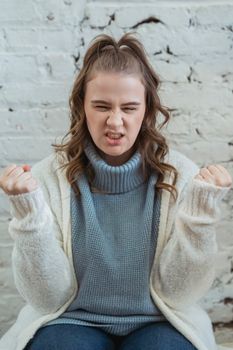 Tensive female in warm sweater sitting on bench and clenching fists and grinning