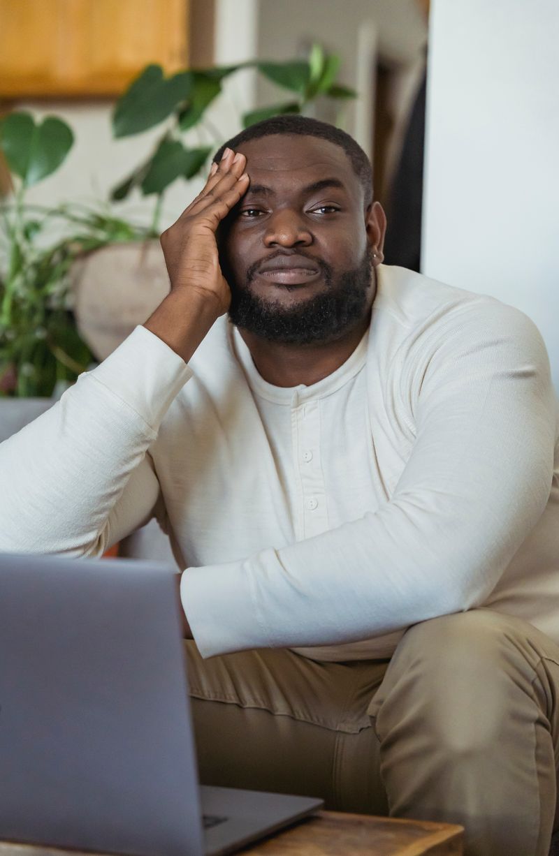 A Black man rests his head on his hand, looking fatigued. Sudden fatigue, dark urine, and jaundice are warning signs of a hemolytic episode in people with G6PD deficiency.