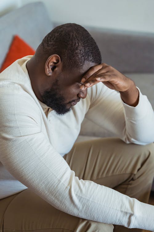 Pensive black man sitting on sofa with bowed head