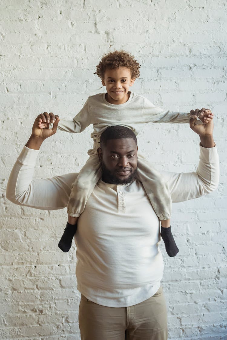 Cheerful Black Father Carrying Son On Shoulders