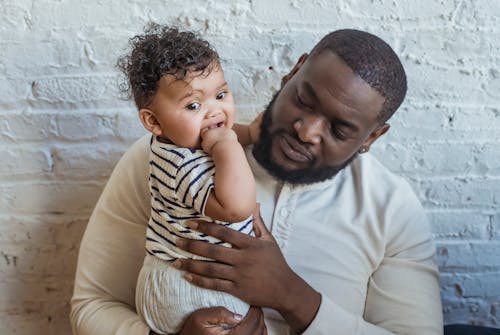 Free Content African American father in casual wear with cute little black toddler in arms near white wall in light room Stock Photo
