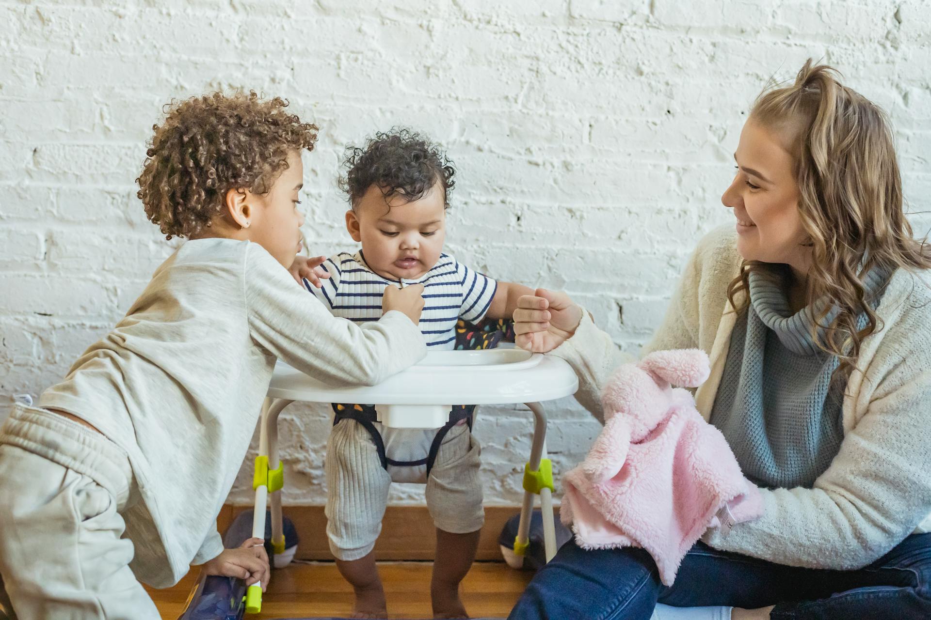 A joyful family scene featuring a mother bonding with her baby and older sibling indoors.