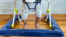 Unrecognizable barefoot African American toddler in casual clothes sitting in baby walker near white wall in light room at home