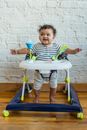Full body of adorable barefoot African American child looking away while sitting in baby walker near wall at home