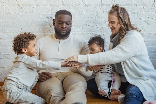 Free Positive multiracial parents playing game with adorable black boy and toddler while sitting on floor near wall in light room Stock Photo