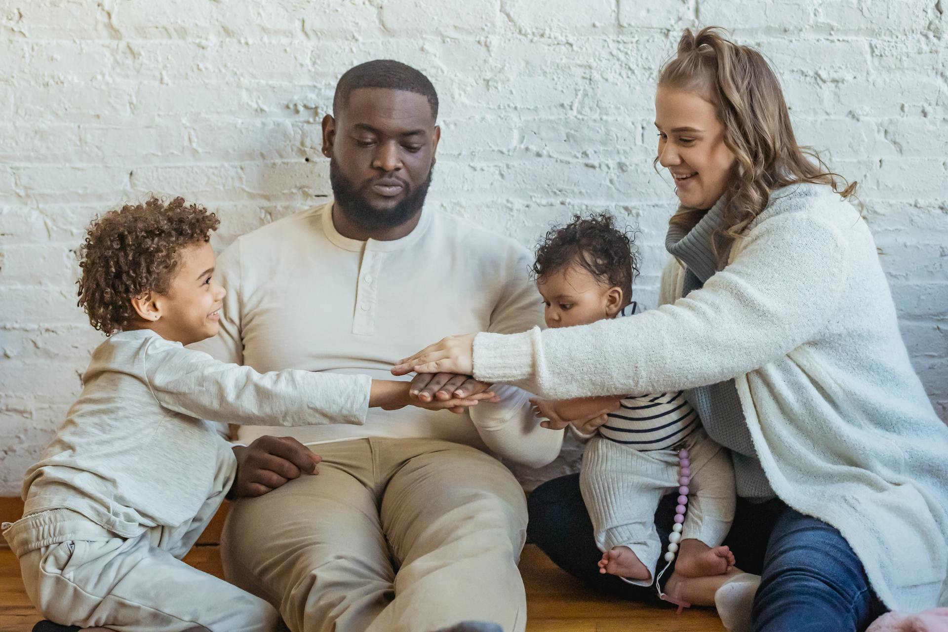 Positive multiracial parents playing game with adorable black boy and toddler while sitting on floor near wall in light room